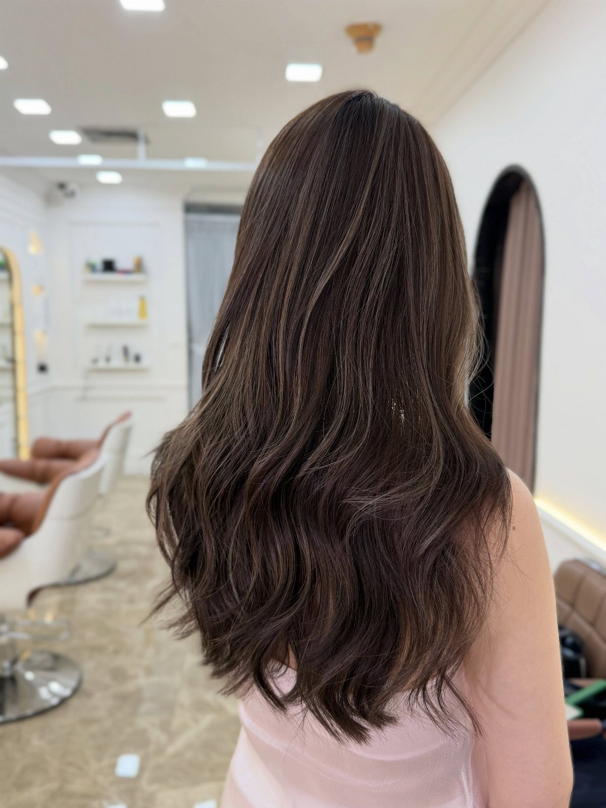Long smoky brunette waves with subtle cool-toned highlights in a bright salon