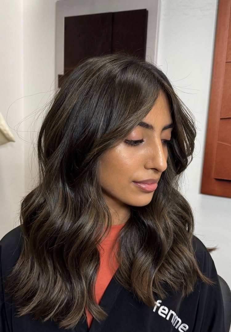Woman with glossy, dark brown wavy hair wearing an orange top and black jacket
