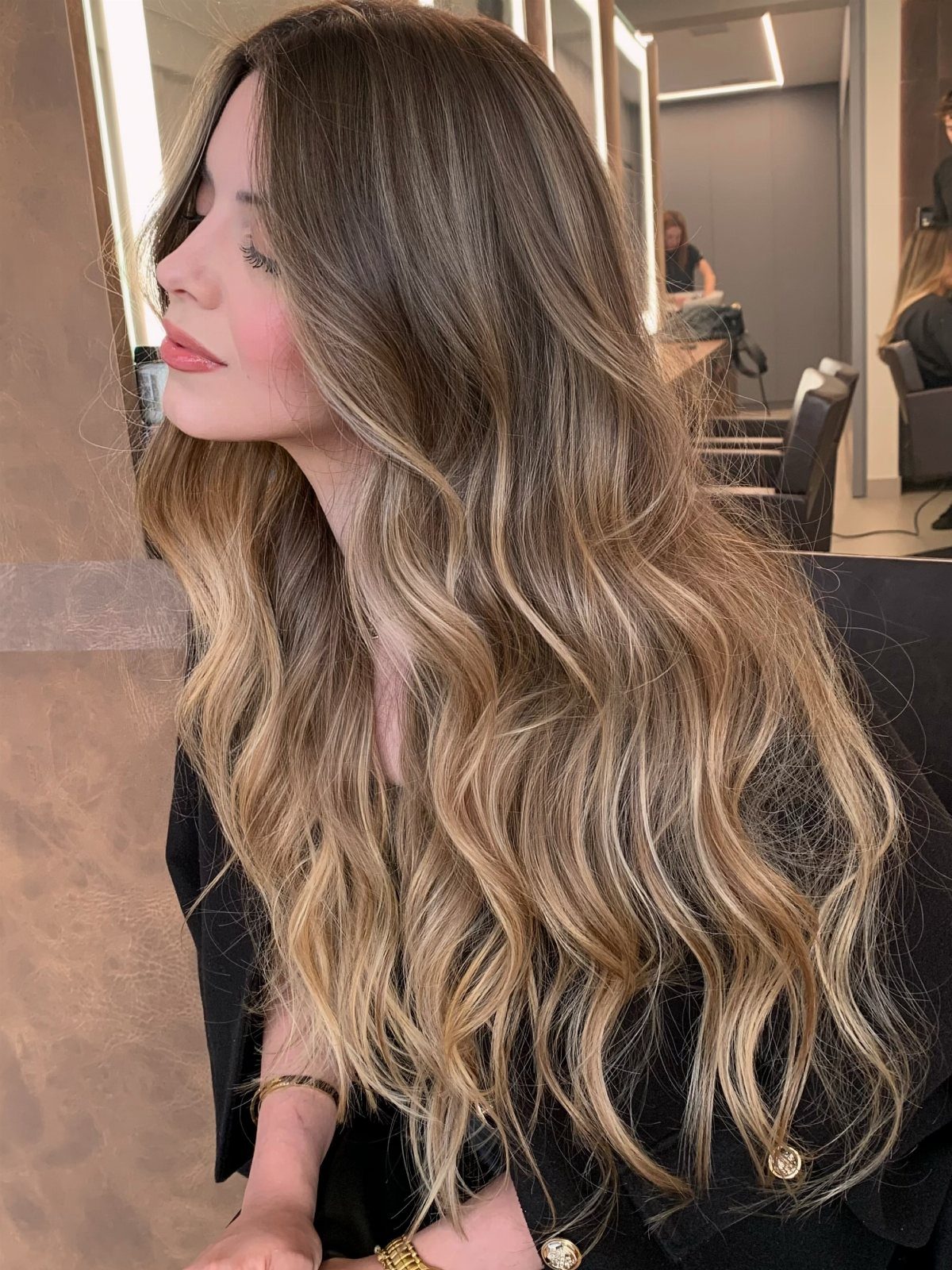 Long wavy brunette hair with golden-brown highlights in a salon