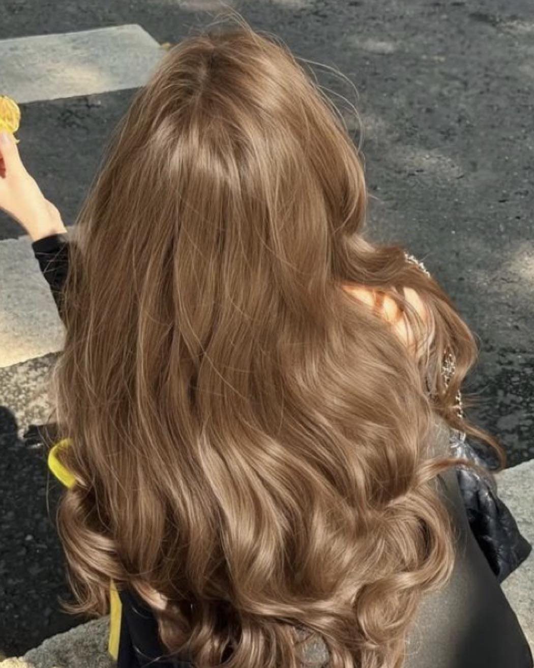 Long wavy golden-brown hair shines in sunlight against dark pavement