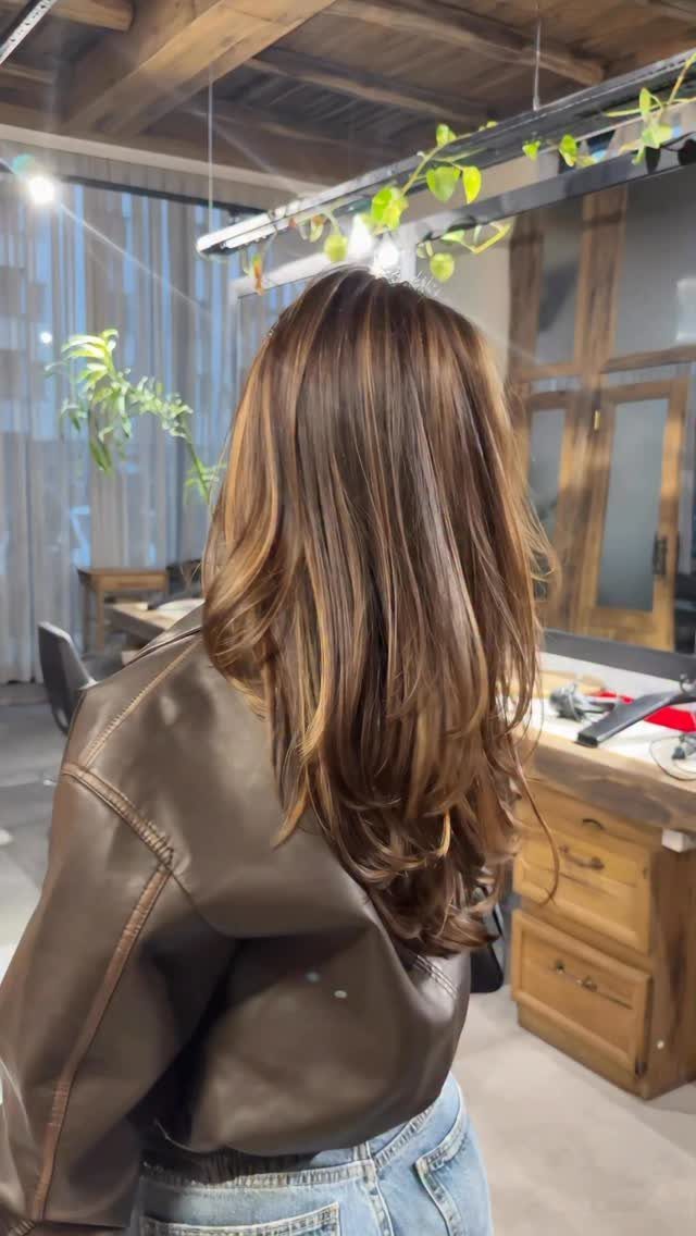 Long wavy brown hair with warm lighter dimension shown from behind in a salon