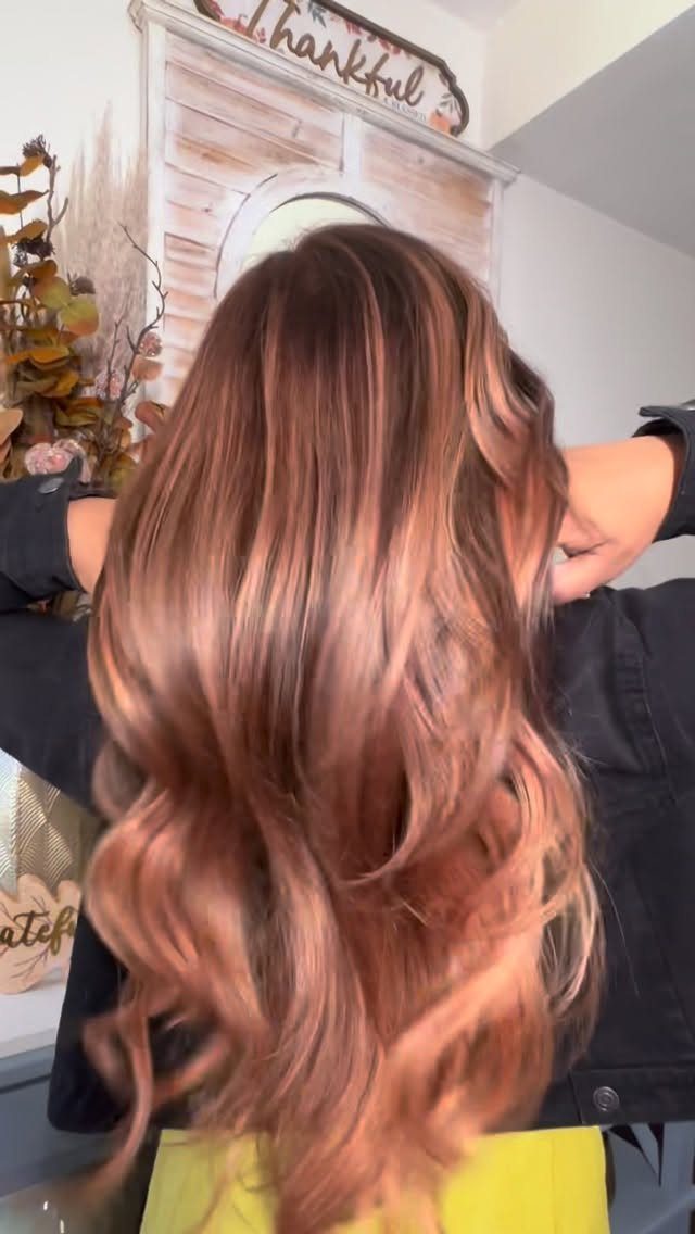Long wavy brown hair with strawberry-copper tones shown from behind in a salon