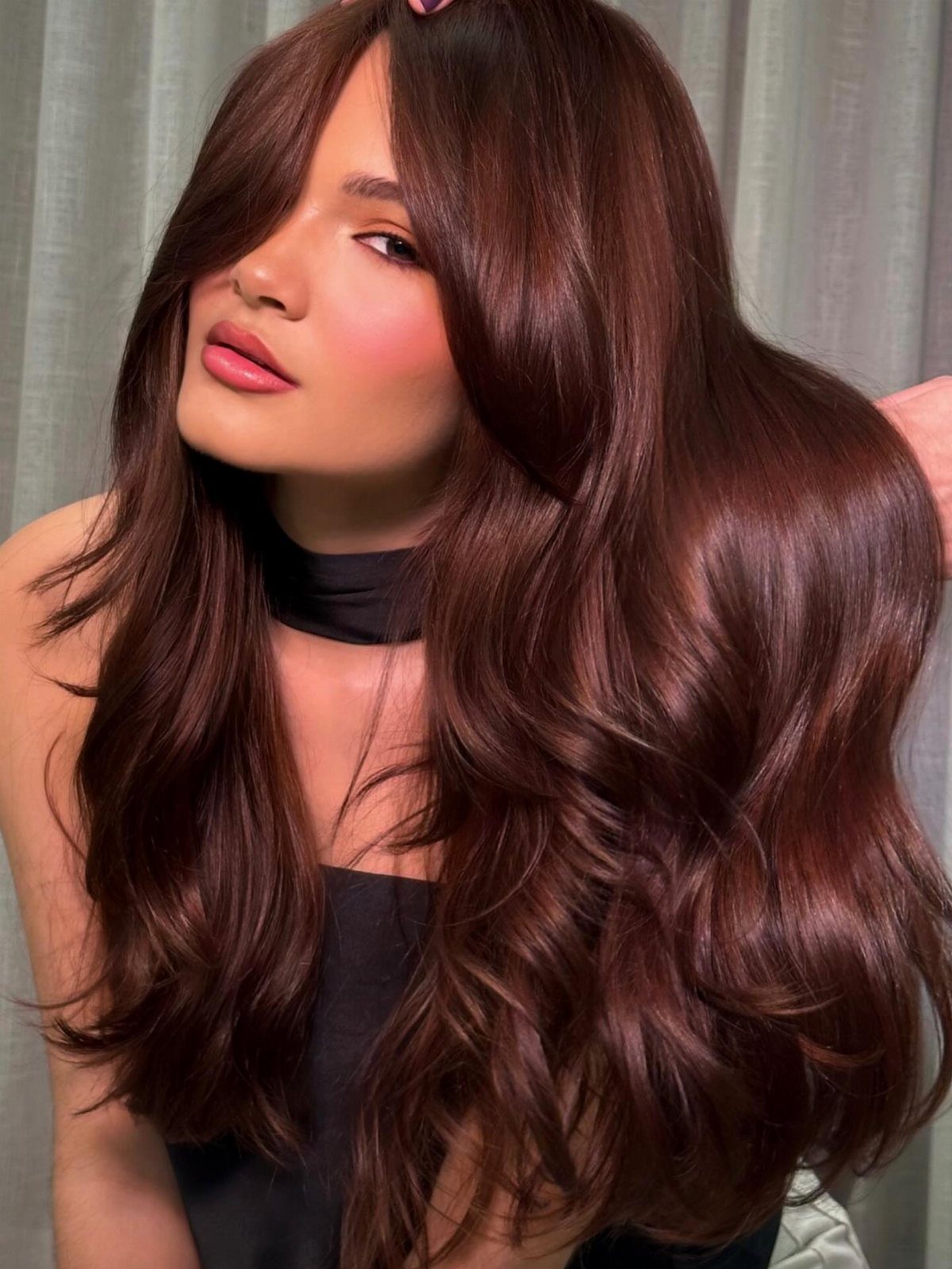 Woman with long, glossy chestnut-brown hair and sweeping layered bangs