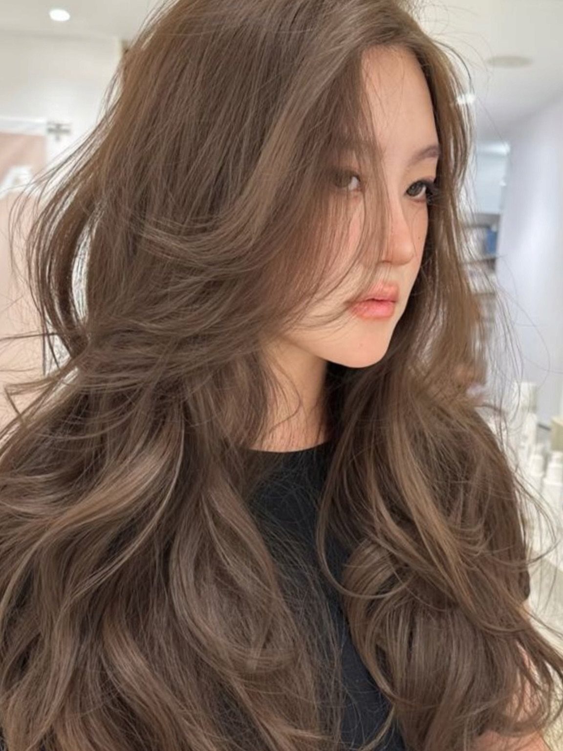 Woman with long, wavy ash brown hair posing in a bright salon