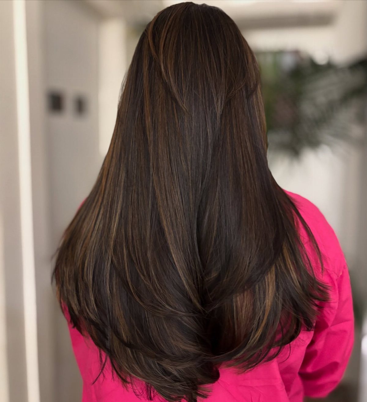 Long dark brown layered hair with subtle lighter strands over a bright pink top