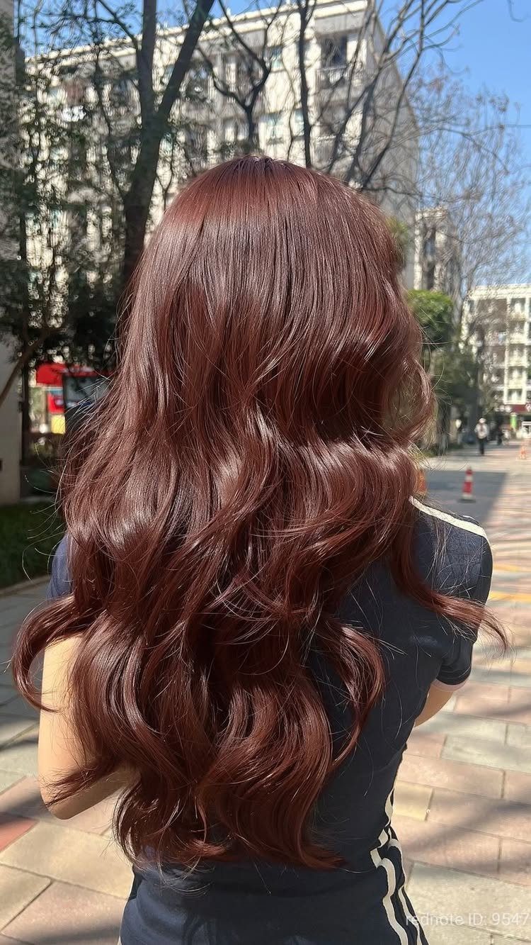 Long wavy reddish-brown hair shines in sunlight against a city street