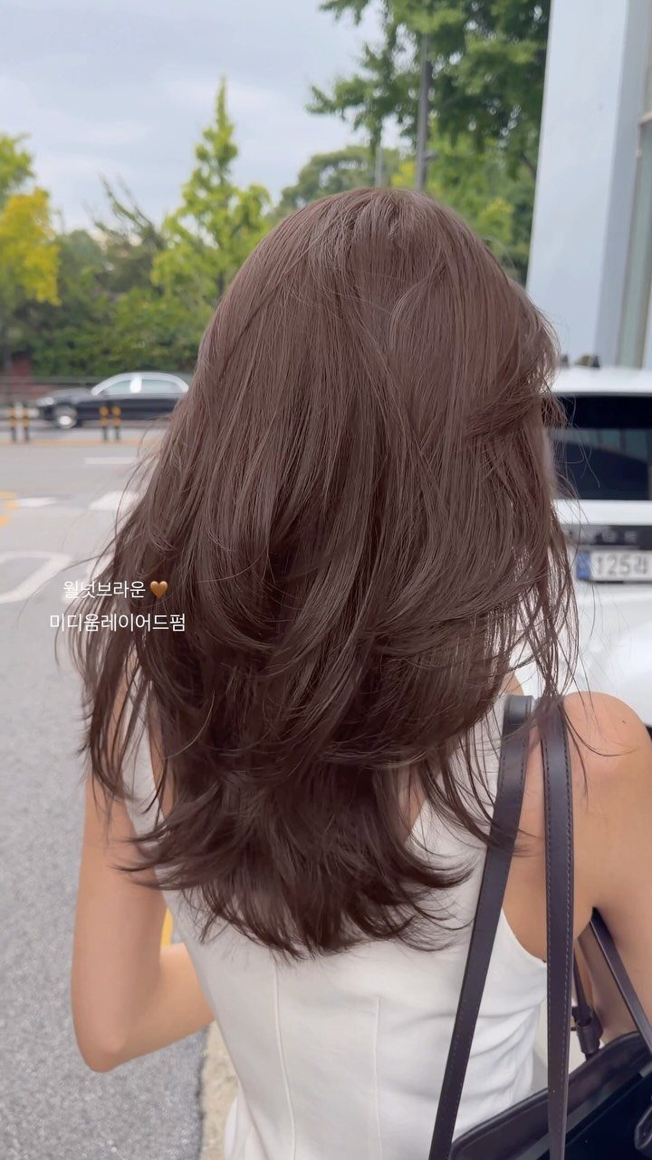 Layered medium brown hair falls over a white sleeveless top