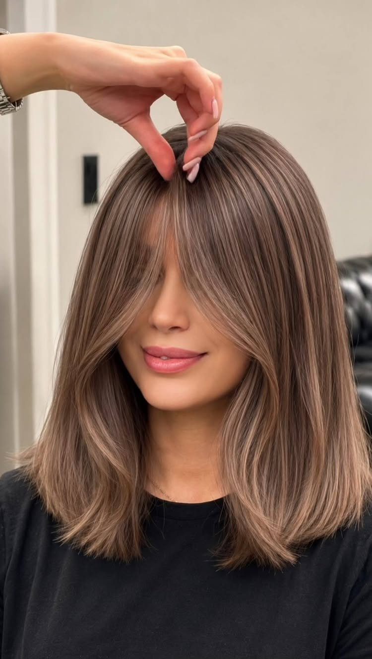 Smoky brown shoulder-length hair with curtain bangs styled in a salon
