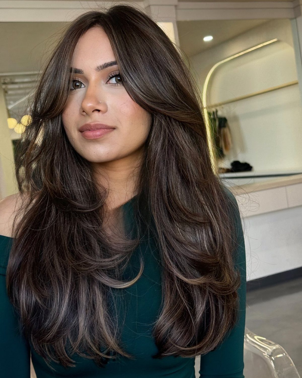Woman with long, cool-toned dark brown layered hair and soft waves in a salon