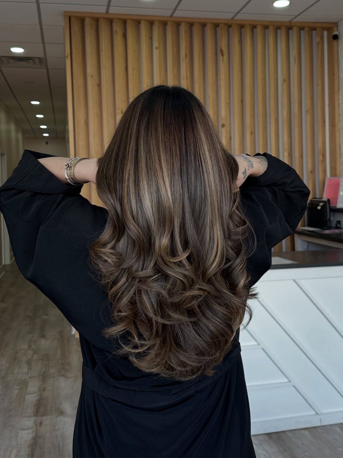 Long wavy dark brunette hair with subtle warm golden-brown highlights in a salon
