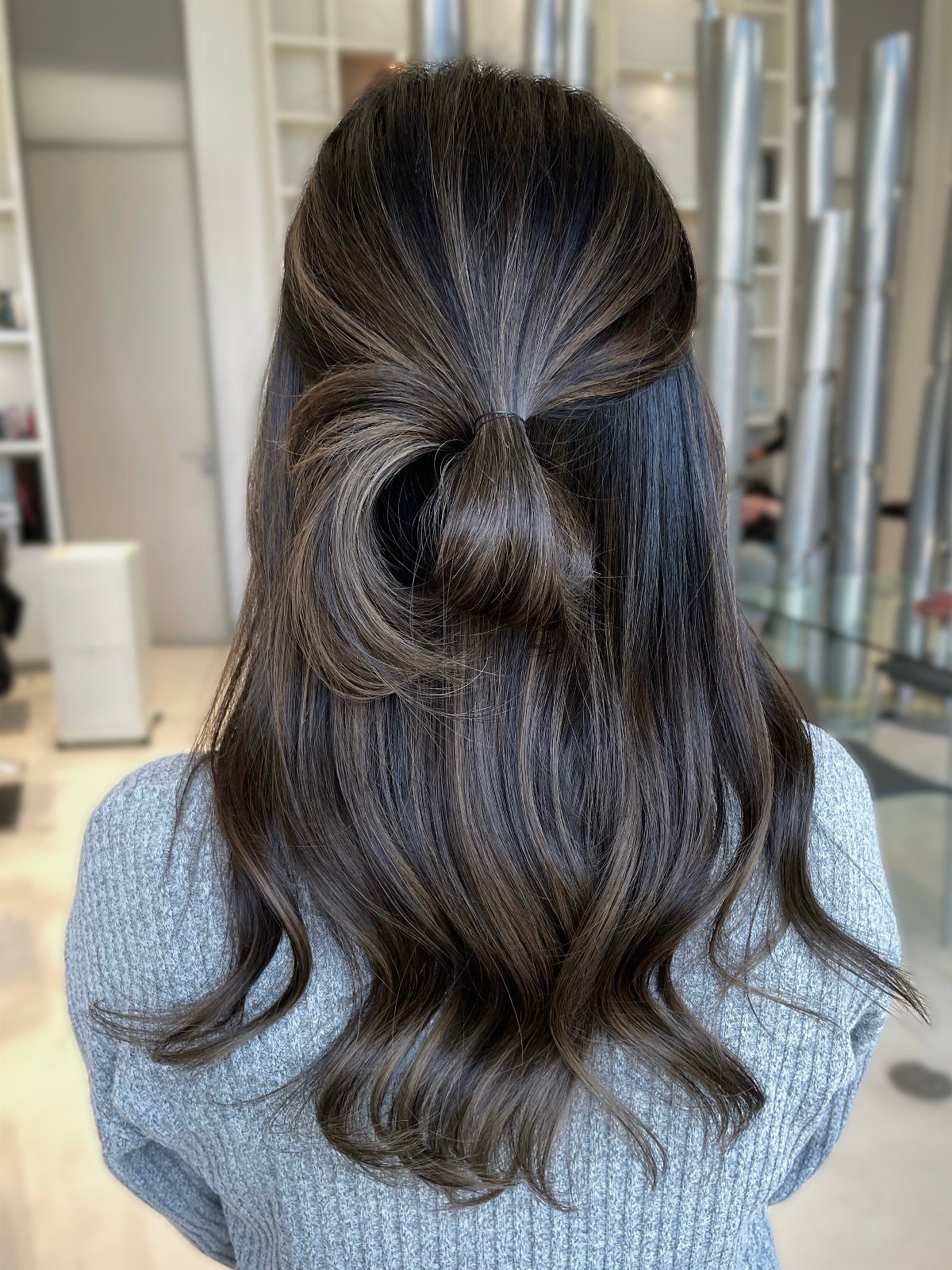 Long brunette waves with cool charcoal highlights styled half-up in a loose bun