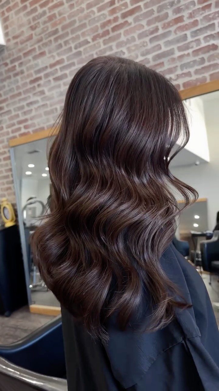 Glossy dark chocolate brown hair styled in long, loose waves in a salon