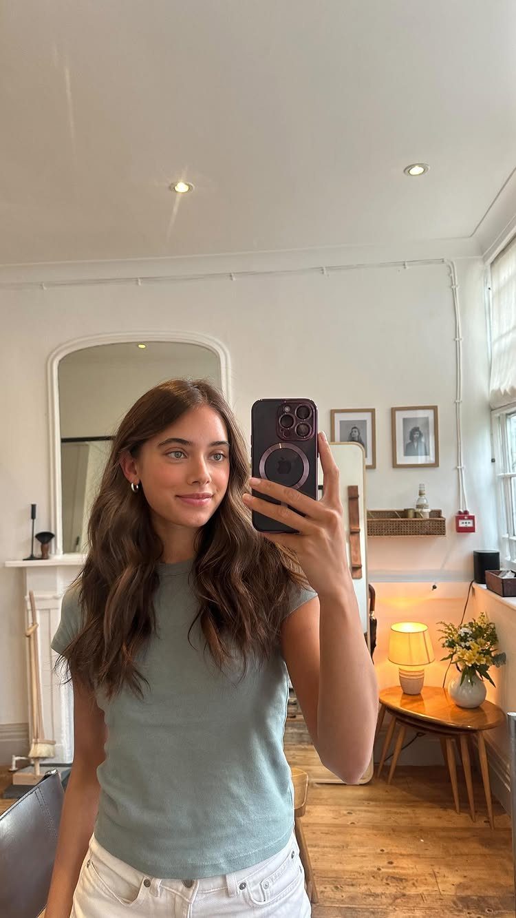 Woman with long, wavy dark neutral brunette hair taking a mirror selfie