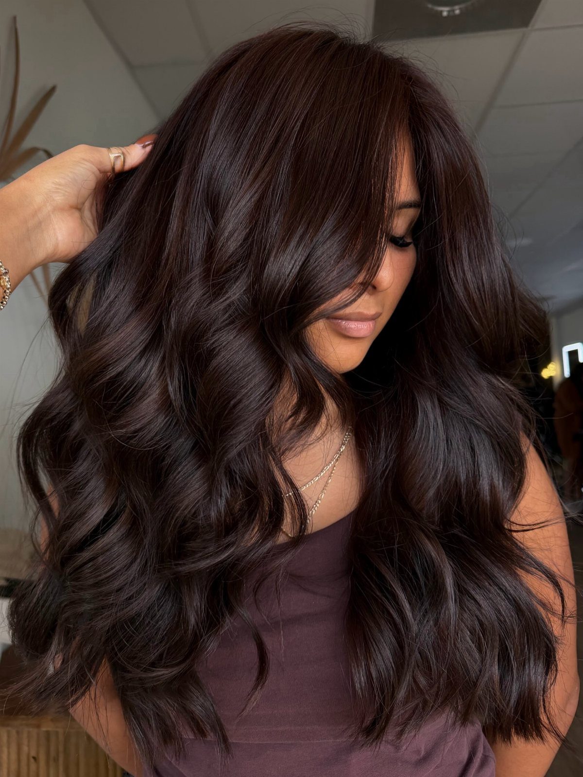 Long glossy dark brown waves frame a woman’s face indoors