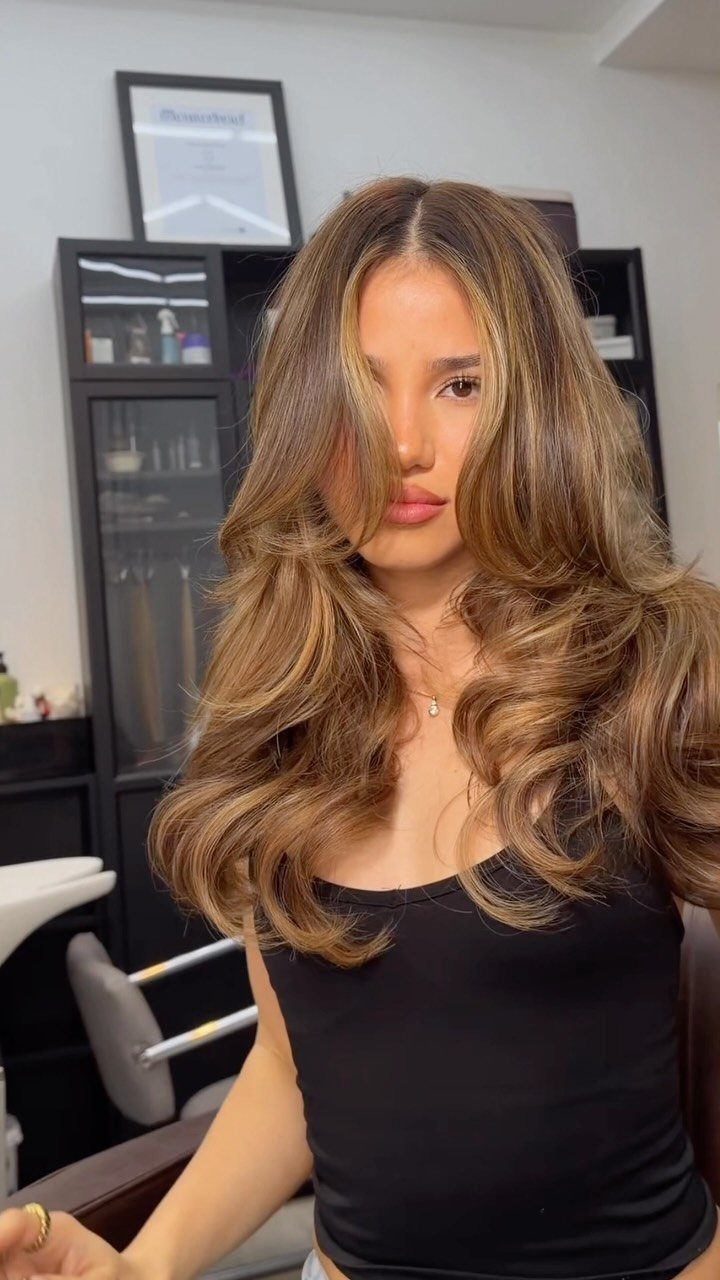 Woman with voluminous brown waves and warm caramel highlights in a salon