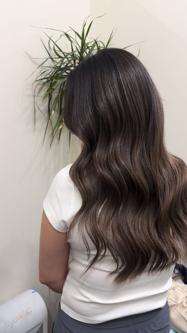 Long muted ash-brown waves fall down the back of a person in a white top