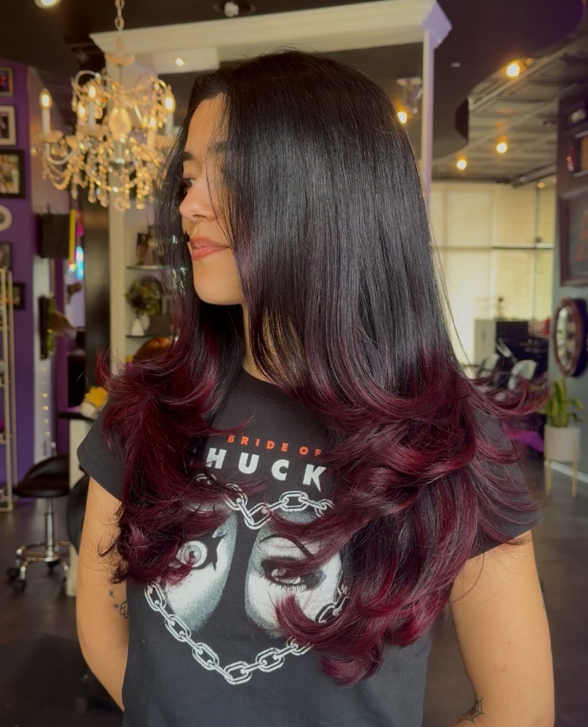 Woman with dark hair and deep burgundy-red curled ends in a salon