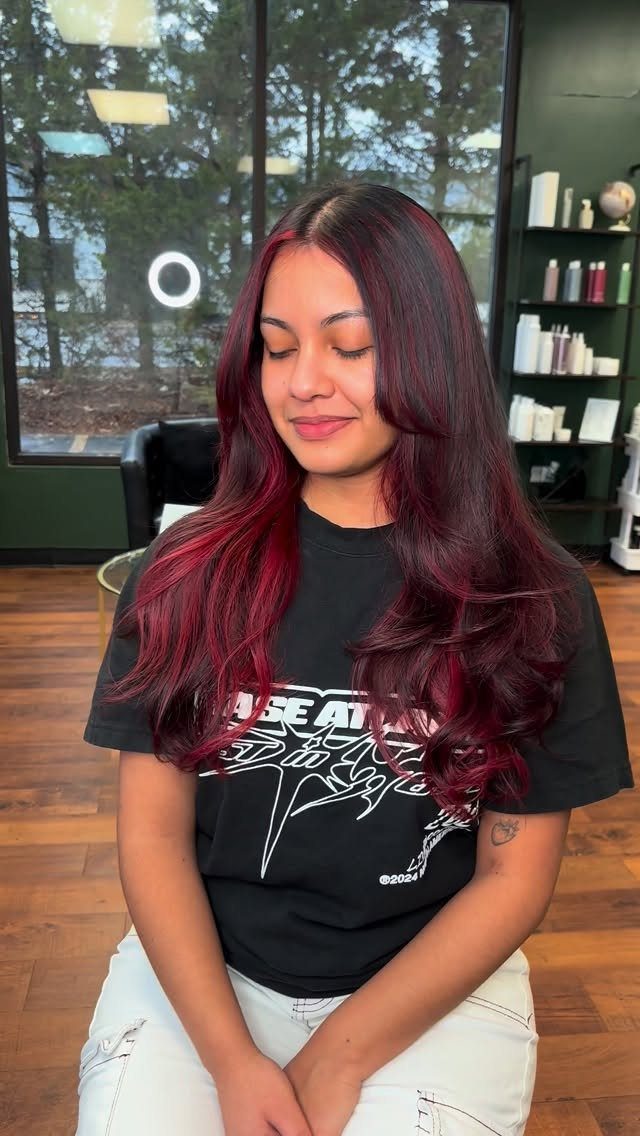 Woman with long wavy dark red balayage hair seated in a salon