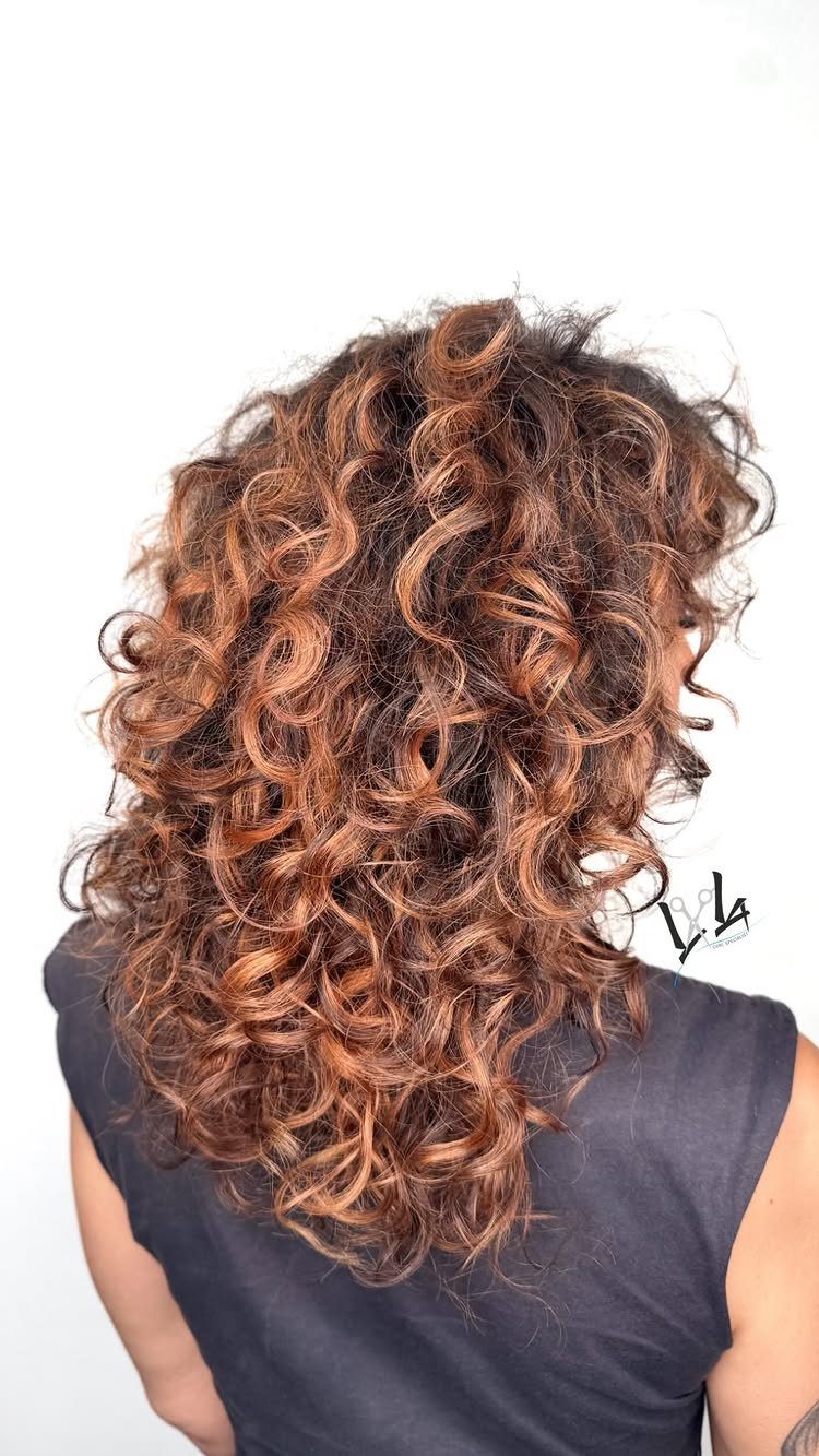 Curly auburn hair with copper highlights cascading over a dark sleeveless top