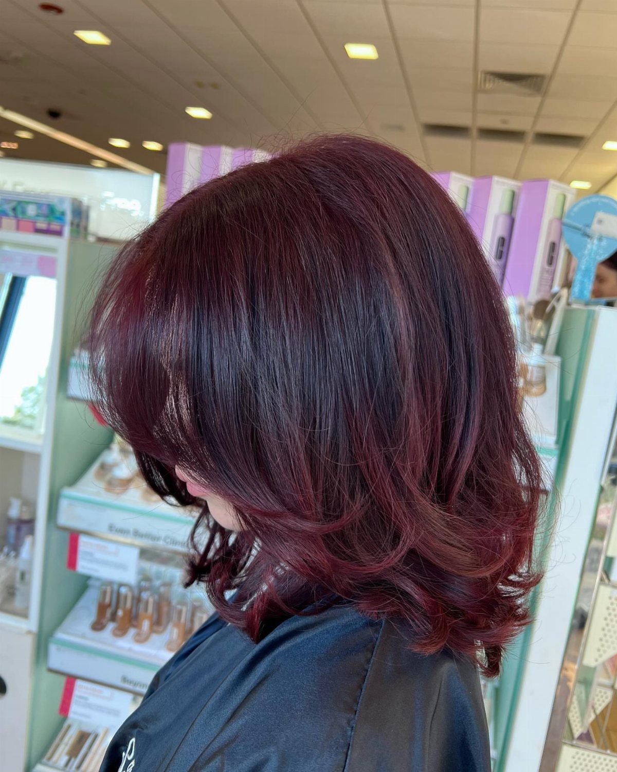 Layered burgundy-red hair with subtle dark tones shown from behind in a salon