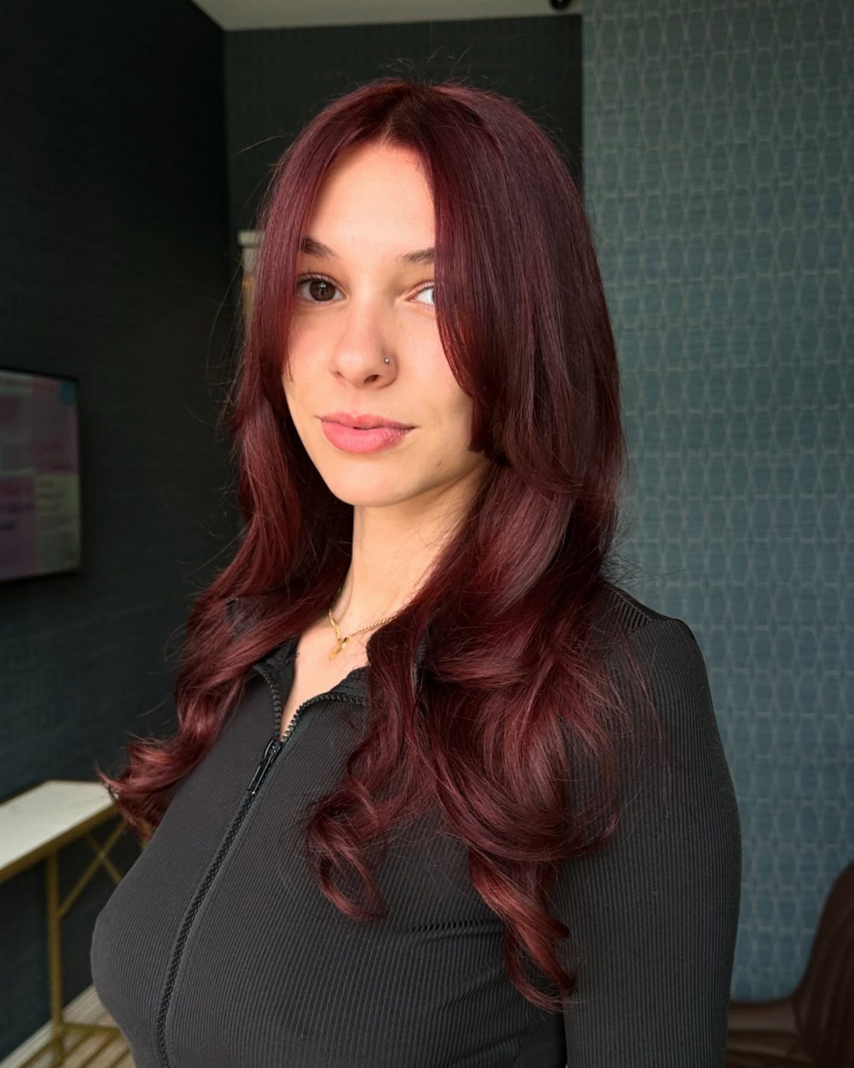 Woman with long, glossy deep auburn-red hair styled in loose curls