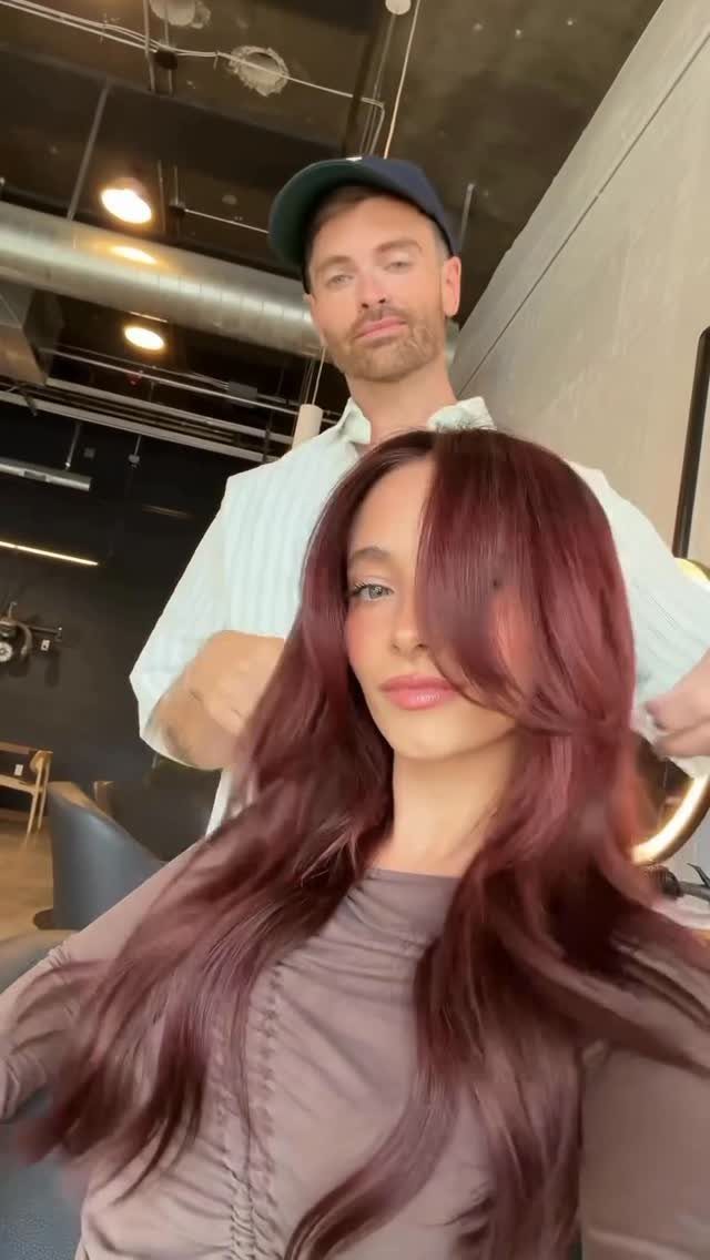 Woman with long, glossy dark cherry-red hair in a salon chair