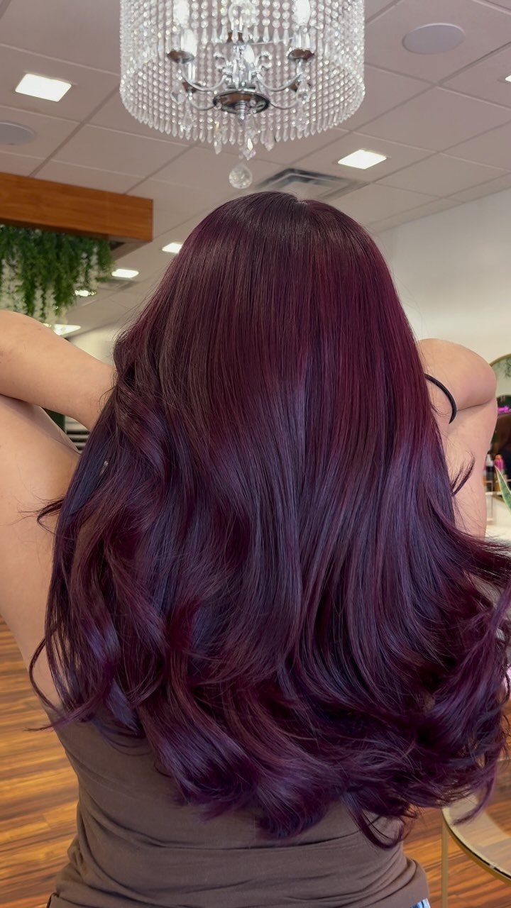Long aubergine-red layered hair with glossy, loose curls in a salon