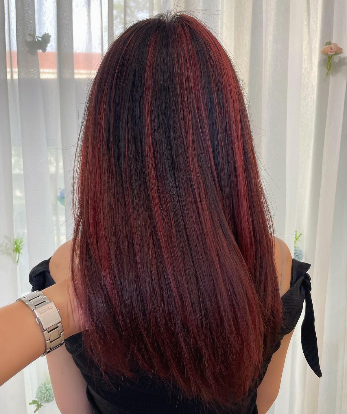 Long dark red hair with ruby and burgundy highlights against white curtains