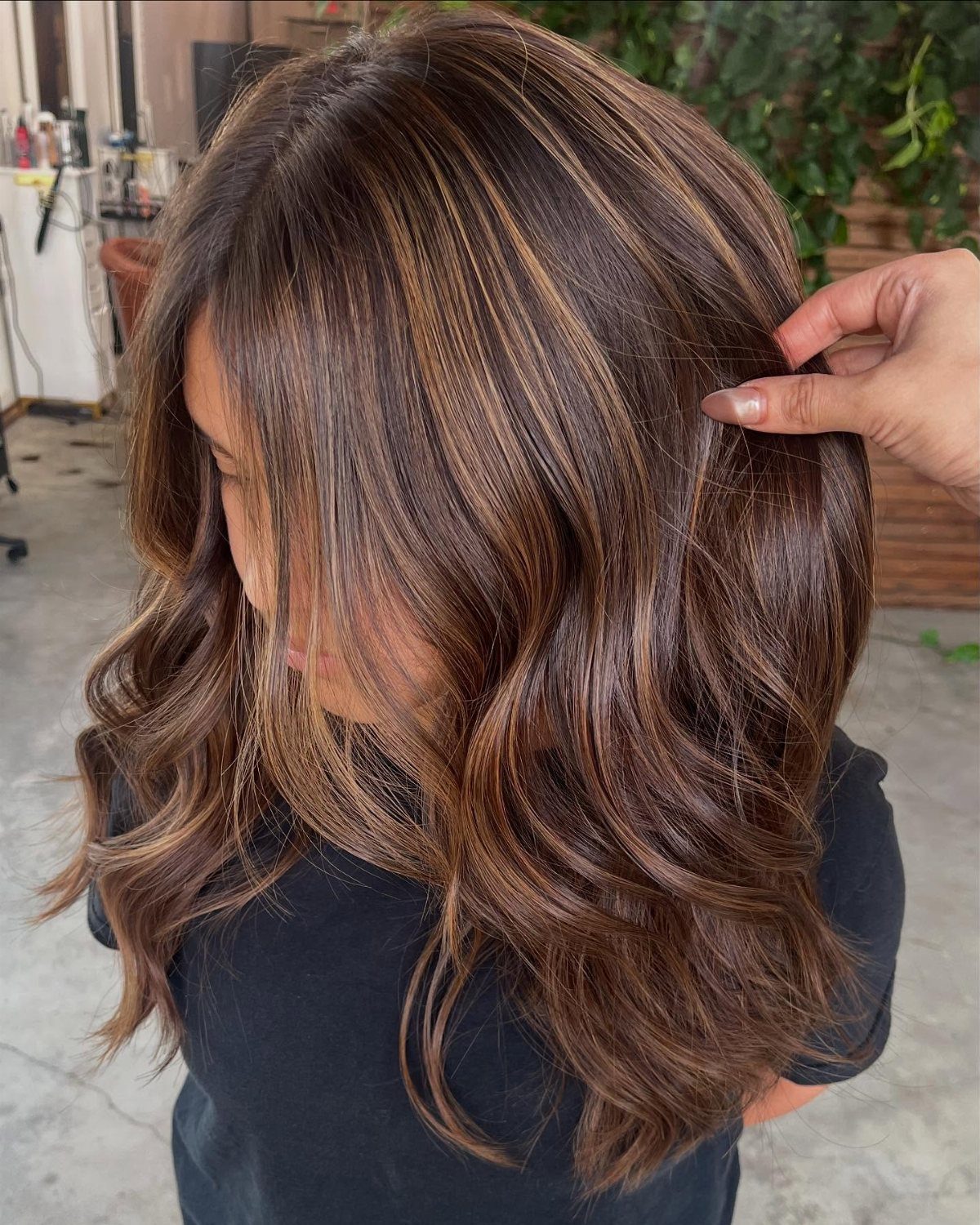 Long brunette curls with warm caramel highlights separated by a hand