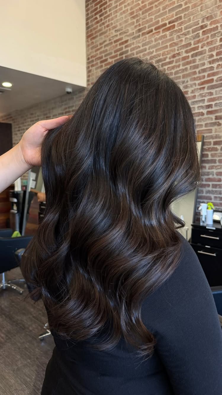 Long, glossy dark brunette hair falls in loose salon-styled waves