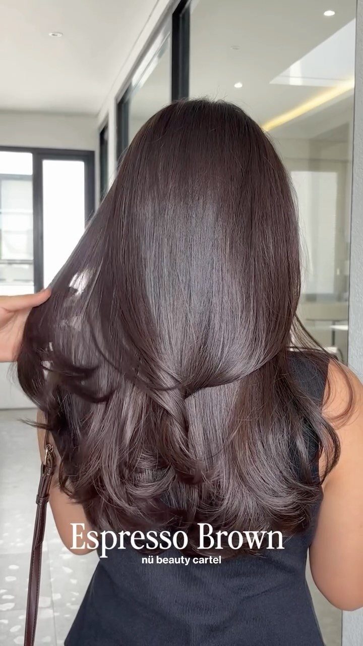 Long espresso-brown hair falls in glossy waves against a bright salon interior.