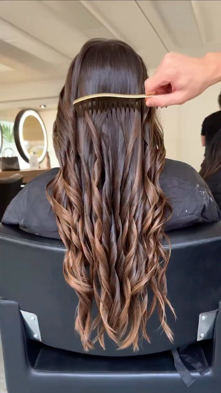 Long wavy brown hair with golden-brown ends being combed in a salon