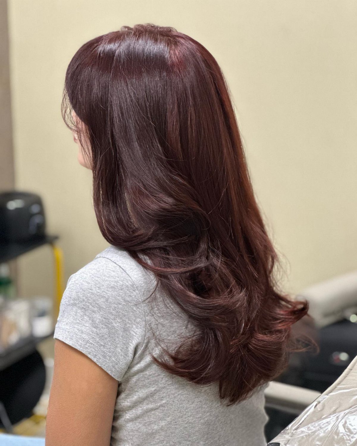 Long mahogany-brown hair with glossy waves and curled ends in a salon