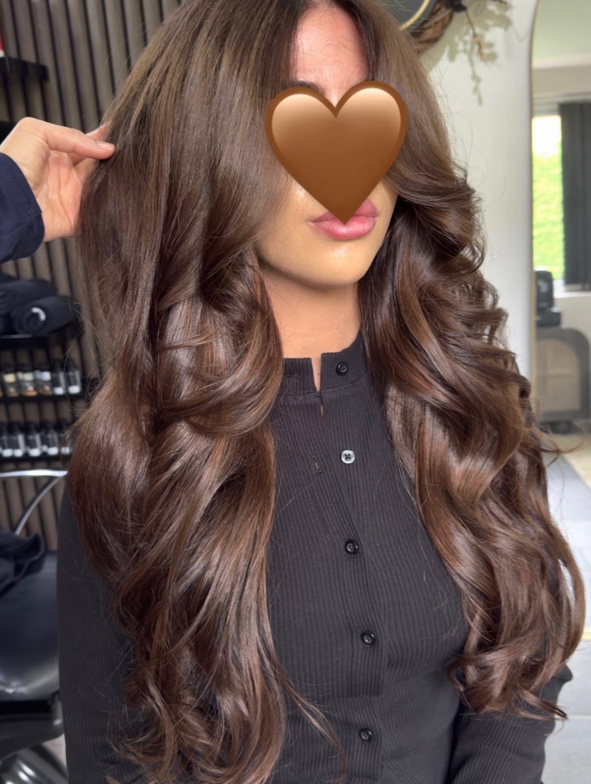 Long cool brown curls frame a woman seated in a salon chair