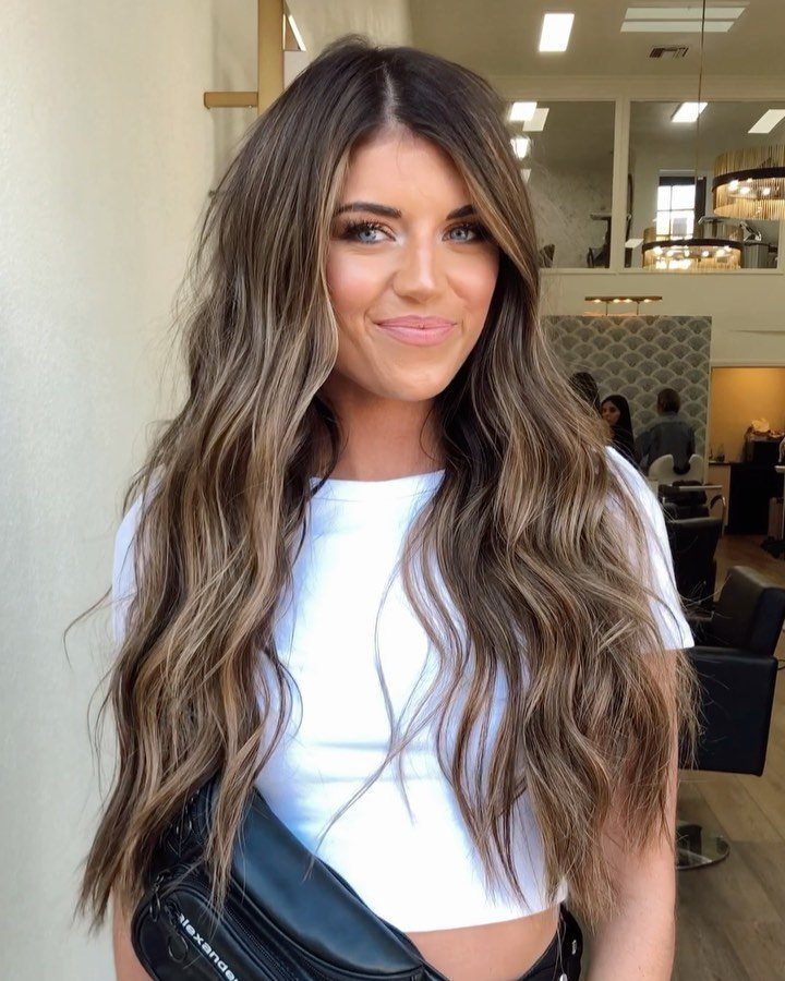 Woman displaying long brunette hair with sunlit lighter streaks and loose waves