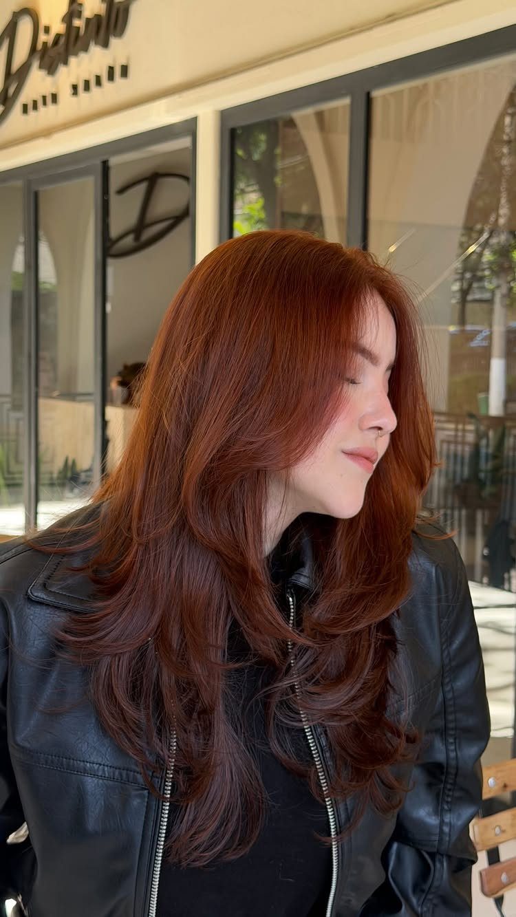 Woman showing long layered auburn hair with warm reddish-brown tones