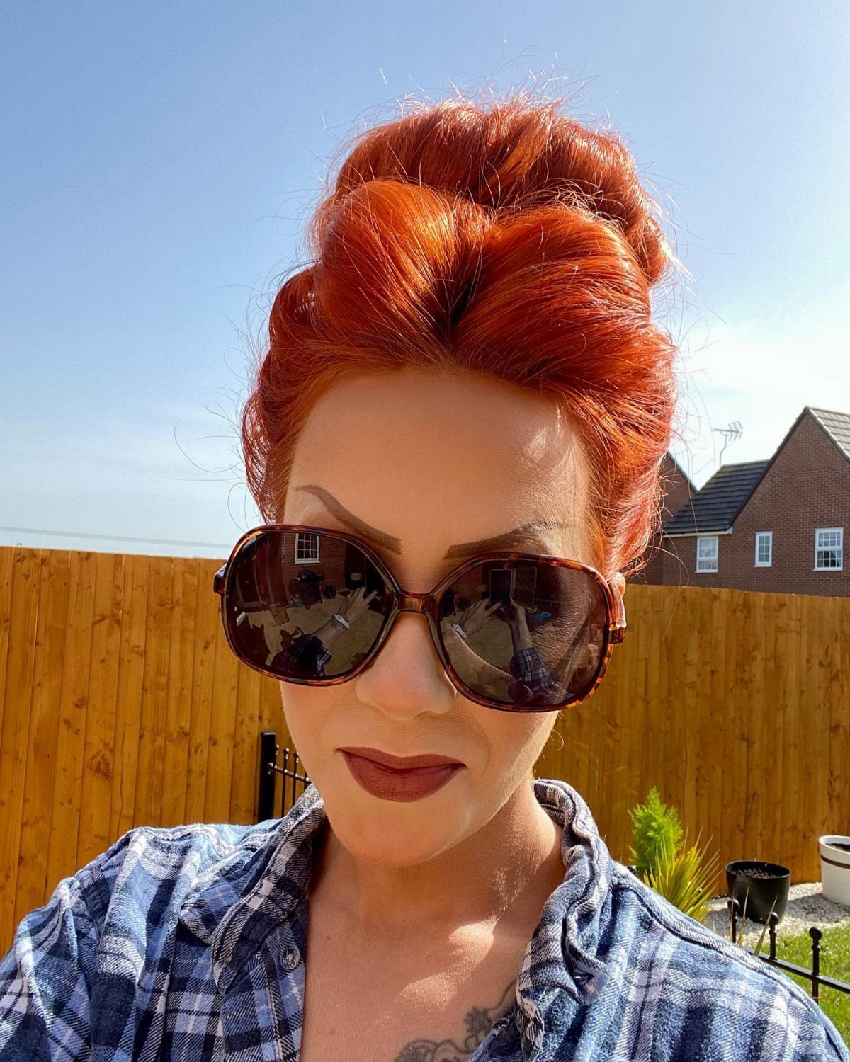 Woman with vivid copper-red hair styled up, wearing sunglasses outdoors
