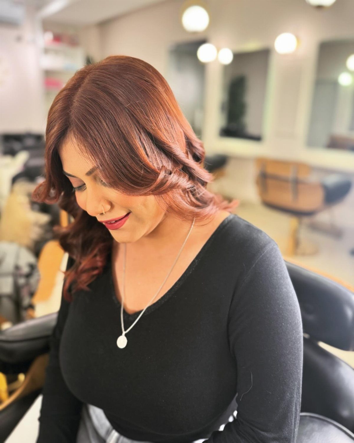 Woman displaying layered brown-red hair with side-swept bangs in a salon