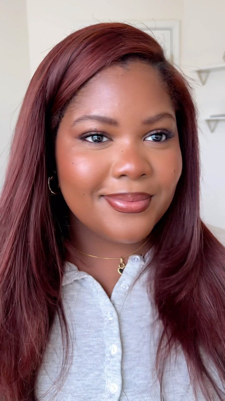 Woman with long burgundy-red hair, light gray shirt, and gold necklace