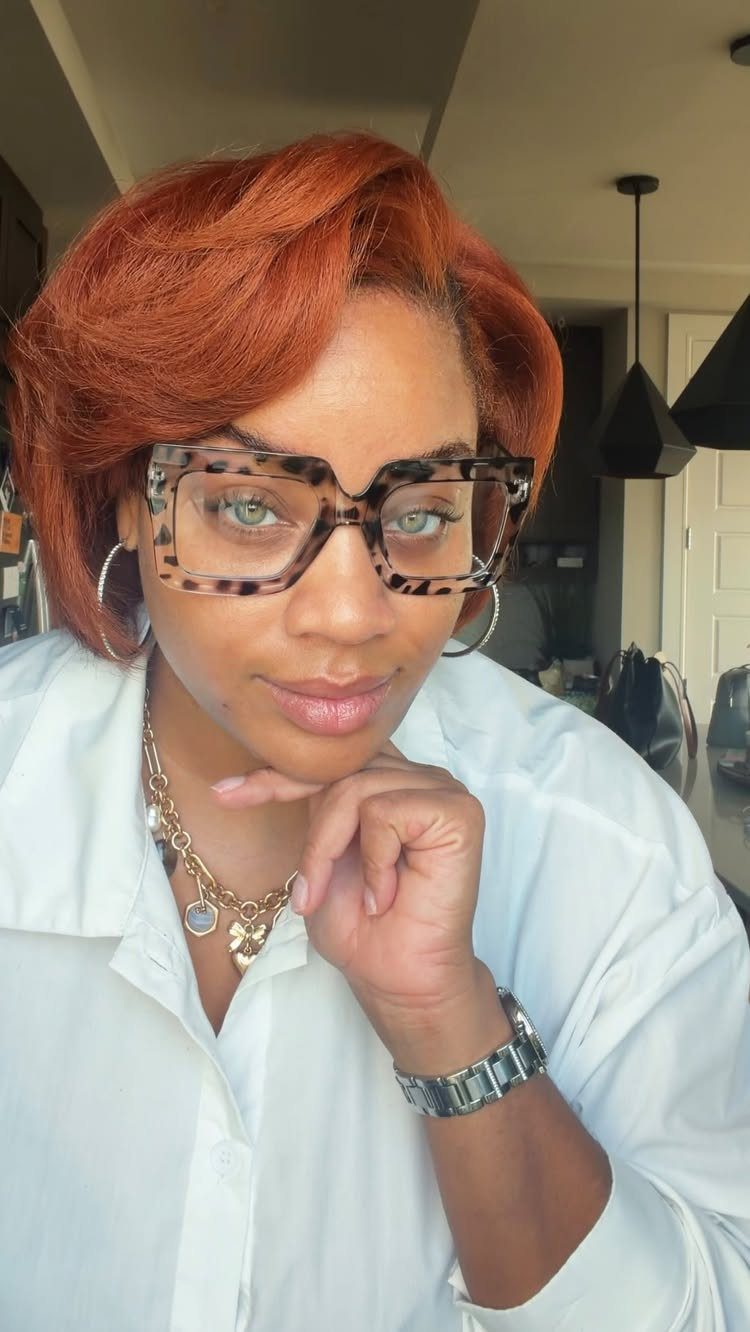 Person with short, voluminous cinnamon-red hair, glasses, and a white shirt