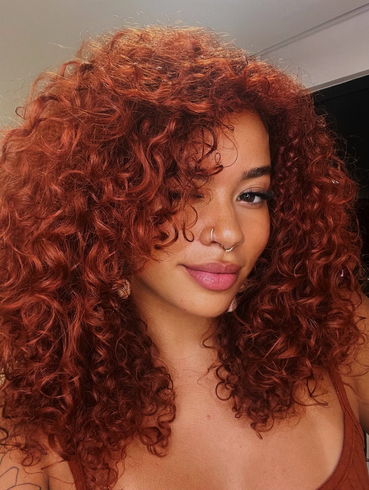Woman with voluminous curly copper-red hair wearing a rust-colored top