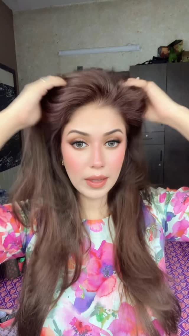 Woman lifts long reddish-brown hair while wearing a bright multicoloured top