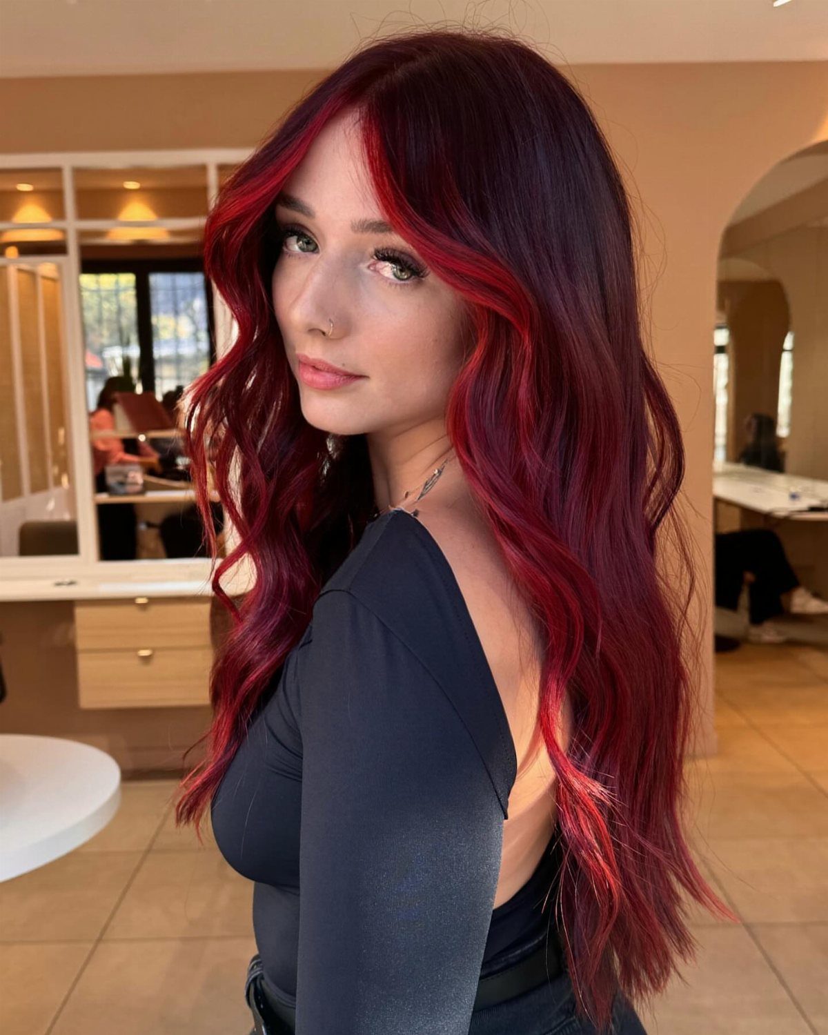 Woman with long dark red hair and vivid red face-framing streaks in a salon