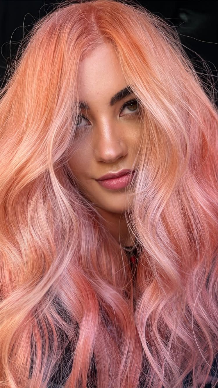 Woman with long, wavy peachy pink-red hair against a dark background