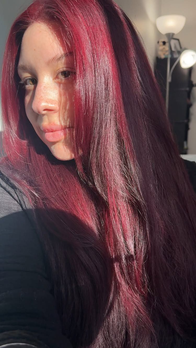 Long burgundy hair with vivid pink-red highlights falls over a black top