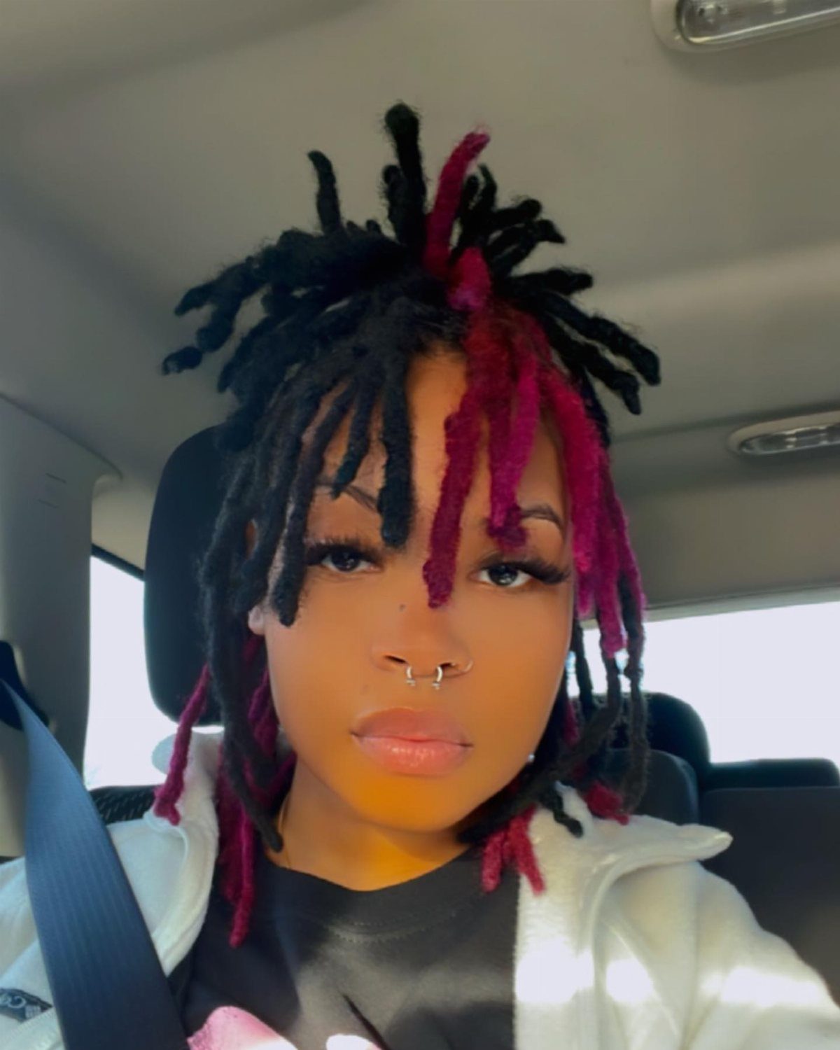 Black and magenta-red locs frame a person’s face inside a car