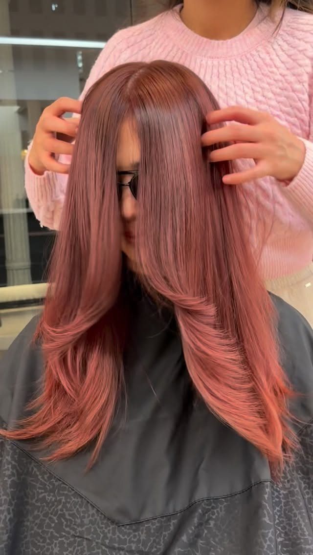 Long rose-pink layered hair with warm coppery highlights shown in a salon