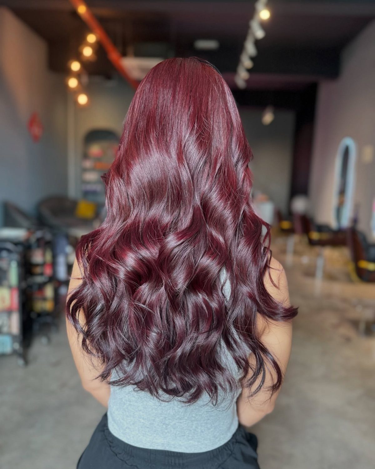 Long glossy ruby burgundy waves shown from behind in a softly lit salon
