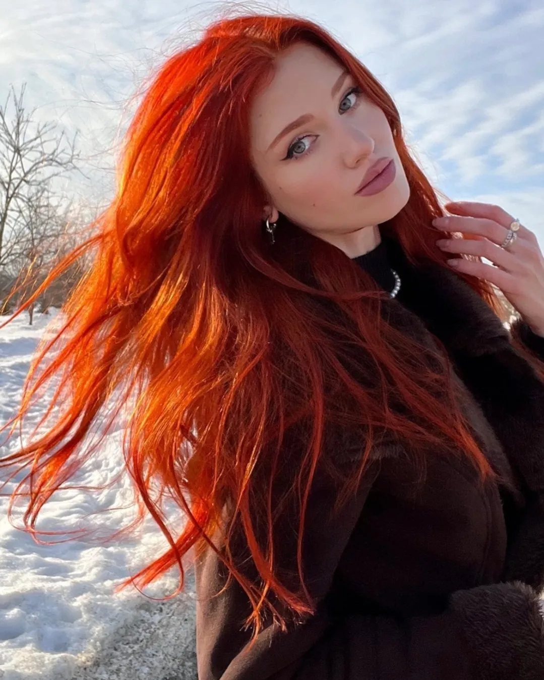Woman with long, vivid scarlet-red hair posing outdoors in snowy surroundings