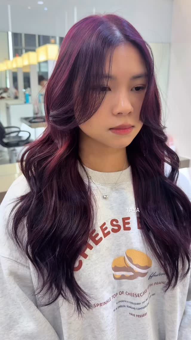 Woman with long wavy violet-red hair seated in a bright hair salon